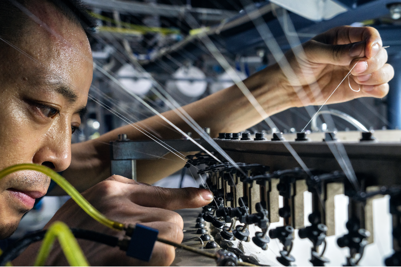 A man threading thin strips of plastic through a device.